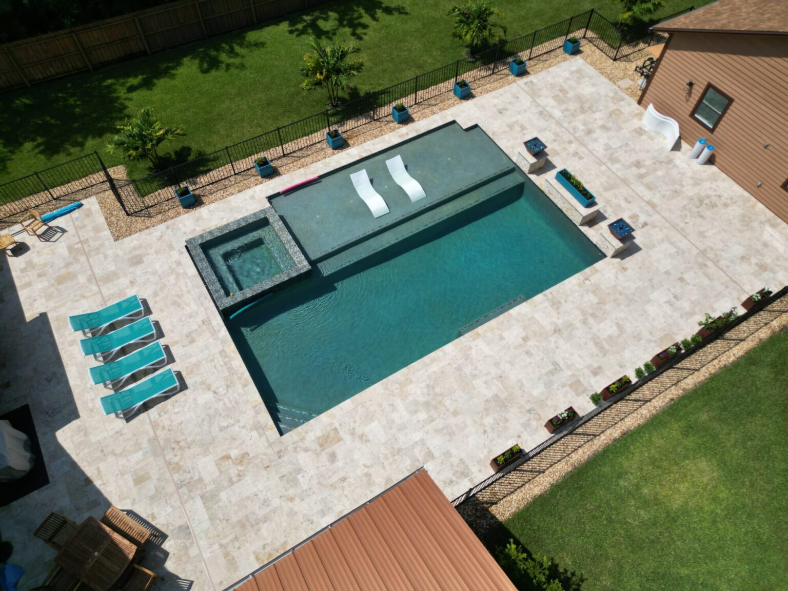 A rectangular pool and spa seen from above, surrounded by a light Keystone Tile travertine pool deck laid in mixed-size pavers