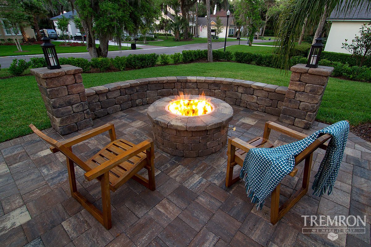 A round Tremron fire pit with two wooden chairs, set inside a curved seat wall on a concrete paver patio